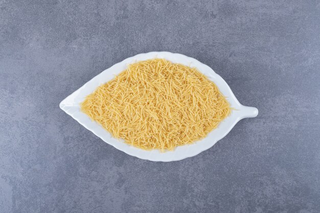 Tas de macaronis crus sur plaque en forme de feuille.