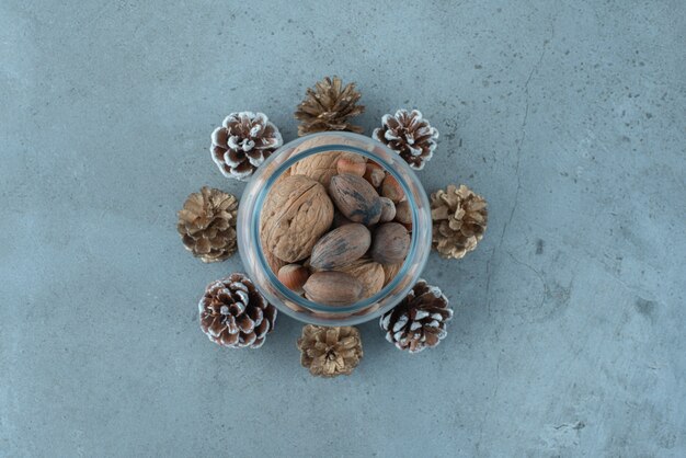 Photo gratuite tas de noix dans un bocal en verre au milieu de pommes de pin sur la surface en marbre