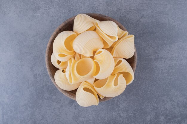 Tas de pâtes en coquille crue dans un bol en bois.