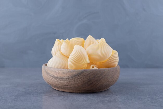 Tas de pâtes en coquille crue dans un bol en bois.