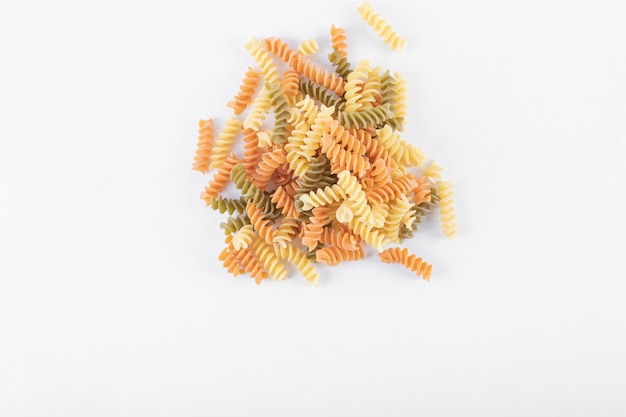 Tas de pâtes fusilli colorées crues sur une surface blanche.