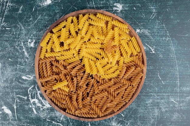 Tas de pâtes fusilli jaunes et brunes sur plaque en bois. Photo de haute qualité