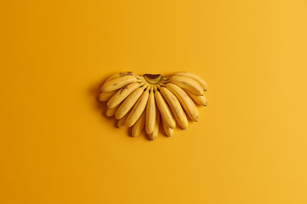 Un tas de petites bananes mûres pour bébés contiennent des nutriments essentiels pour la santé isolés sur fond jaune. Concept de fruits d'été. Mise à plat, vue de dessus. Source naturelle de vitamines. Régime alimentaire et alimentation saine