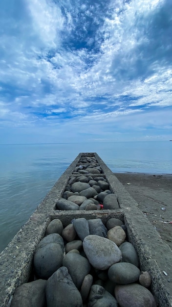 Photo gratuite tas de pierres sur la plage avec ciel bleu et nuages en arrière-plan
