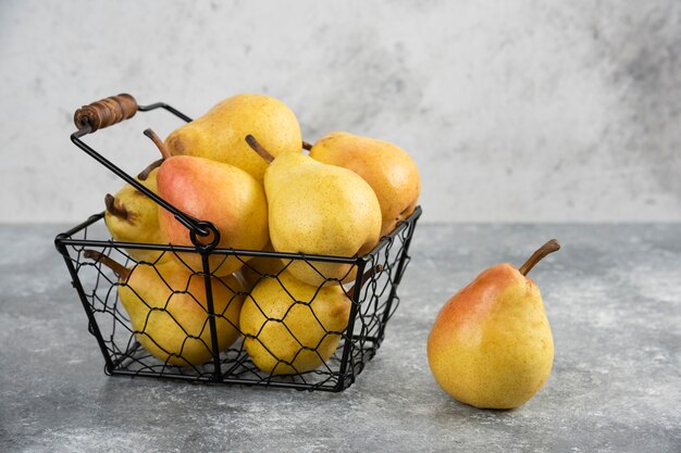 Tas de poires jaunes fraîches dans un seau en métal sur une surface en marbre.