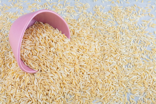 Un tas de riz brun éparpillé et un petit bol sur une surface en marbre