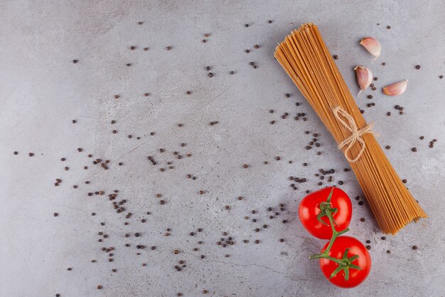 Tas de spaghettis à grains entiers attachés avec une corde et des tomates rouges fraîches.