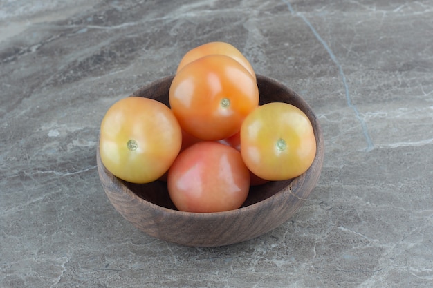 Tas de tomates fraîches dans un bol en bois sur une table grise.