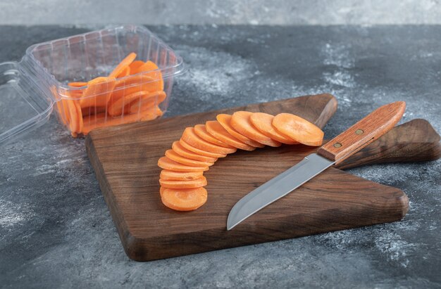 Tas de tranches de carottes sur planche de bois et à l'intérieur d'un récipient en plastique.