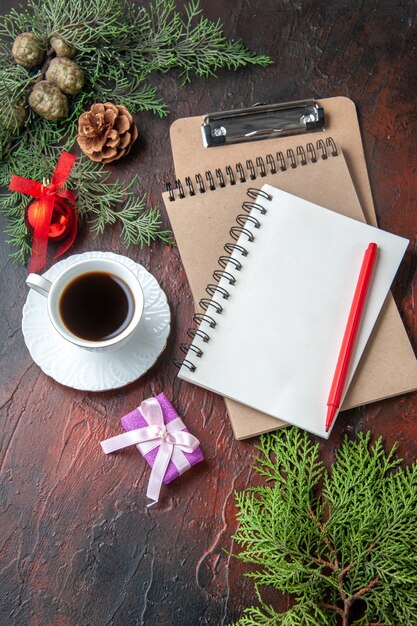 Une tasse d'accessoires de décoration de branches de sapin de thé noir et un cadeau à côté d'un cahier avec un stylo sur des images de fond sombre