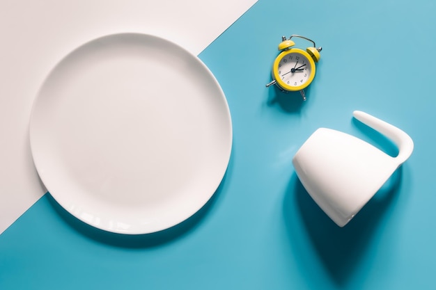 Tasse à assiette vide et réveil sur fond bleu