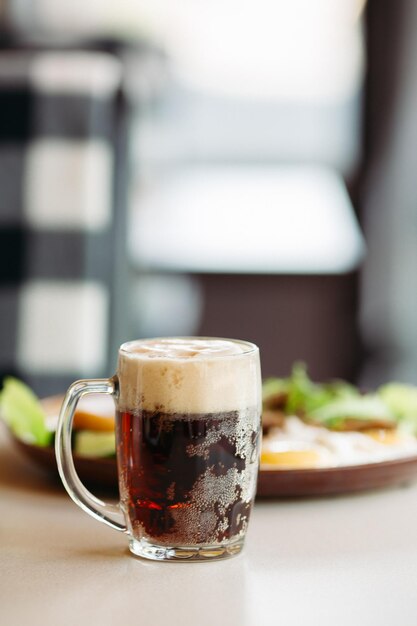 Tasse de bière debout près de l'assiette d'apéritifs Bière brune avec une mousse épaisse et épaisse Debout sur une surface en bois lisse d'une table de restaurant ou de pub Appétissant Froid et frais Pour la compagnie d'amis