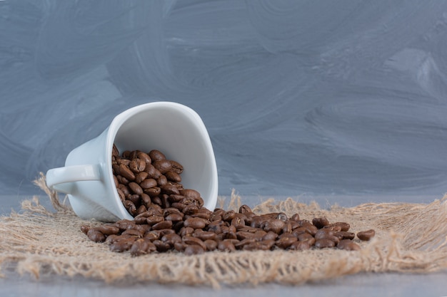 Une tasse blanche de grains de café torréfiés sur fond de marbre.