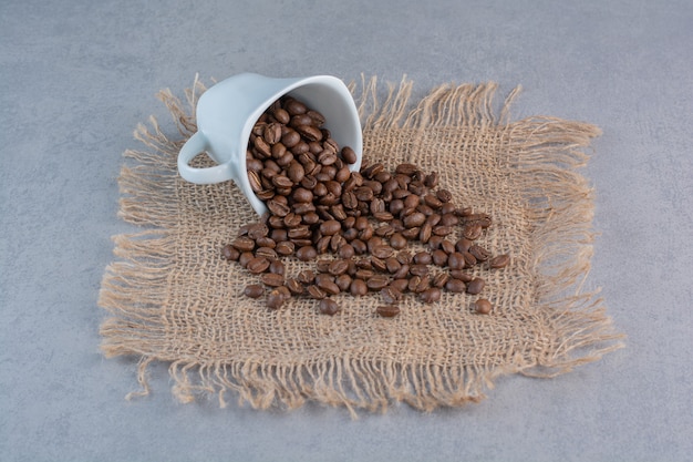 Une tasse blanche de grains de café torréfiés sur une surface en marbre.