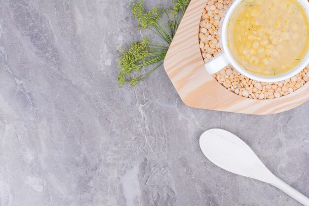 Une tasse blanche de soupe aux pois jaunes dans un plateau en bois.