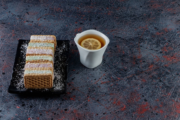 Une tasse blanche de thé chaud avec une assiette noire de gaufres sucrées sur une sombre