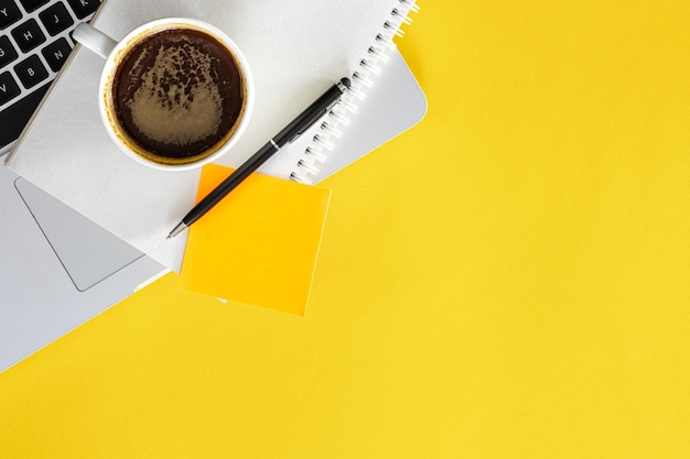 Photo gratuite une tasse de bloc-notes de café et un ordinateur portable sur un fond plat jaune