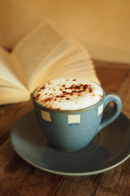 Tasse de café avec beaucoup de mousse et un livre derrière