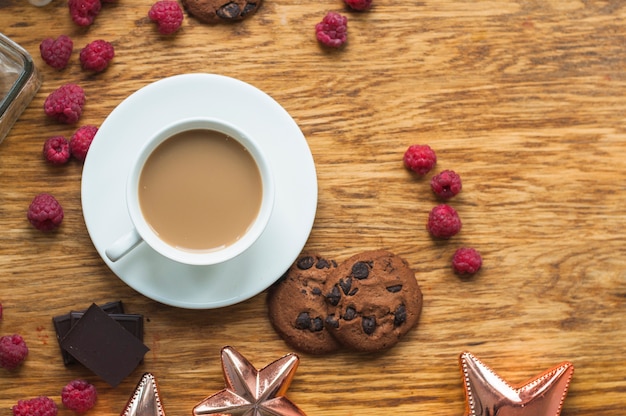 Photo gratuite tasse de café avec des biscuits; framboises et morceaux de barre de chocolat sur une table en bois