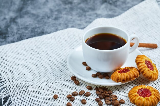 Une tasse de café, des biscuits, des grains de café et de la cannelle.