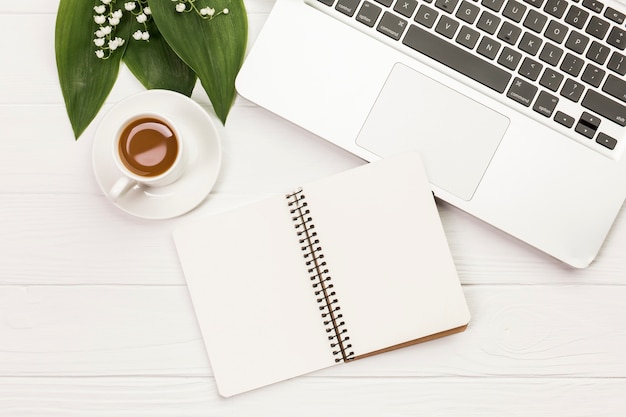 Tasse à café avec bloc-notes en spirale près de l&#39;ordinateur portable sur un bureau en bois blanc