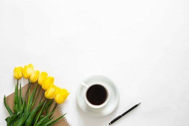 Photo gratuite une tasse de café bouquet de tulipes jaunes et un cahier sur fond blanc