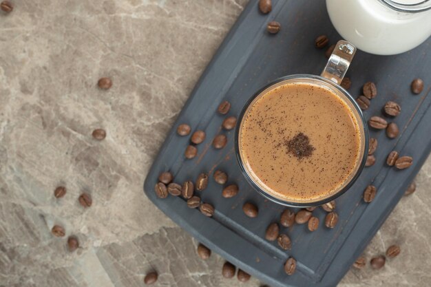 Tasse de café chaud et grains de café sur une assiette sombre.