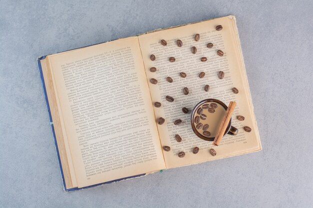 Tasse de café chaud avec des grains de café sur un livre ouvert.