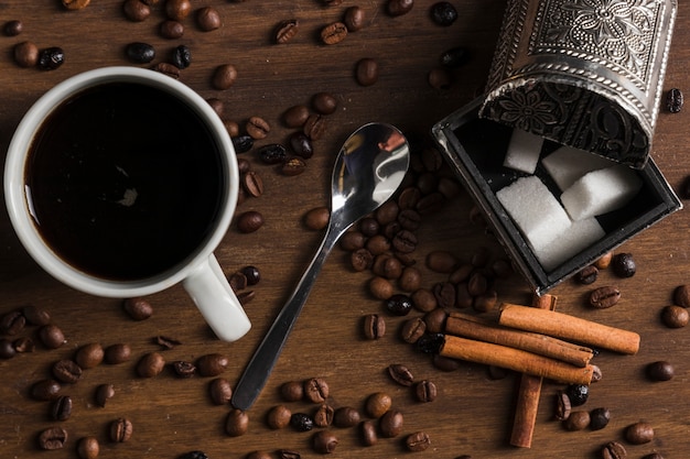 Tasse de café avec une cuillère près de boîte de bâtons de sucre et de cannelle