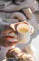 Photo gratuite une tasse de café dans les mains d'une femme sur un fond flou avec un élément tricoté