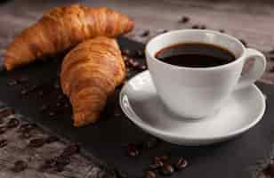 Photo gratuite tasse de café avec une délicieuse pâtisserie et des grains de café étalés. collation du matin.