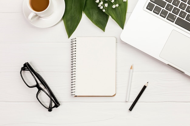 Tasse à café, feuilles, bloc-notes à spirale, lunettes de vue sur le bureau en bois du bureau