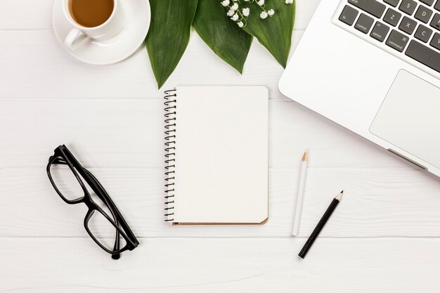 Tasse à café, feuilles, bloc-notes à spirale, lunettes de vue sur le bureau en bois du bureau