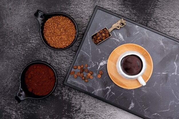 Une tasse de café avec des grains de café dans une cuillère en métal sur une surface sombre