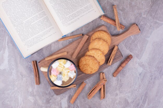 Une tasse de café avec de la guimauve et des biscuits sur planche de bois.