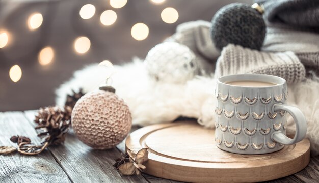 Tasse à café sur les lumières de Noël bokeh à la maison sur table en bois avec pull sur un mur et décorations. Décoration de vacances, Noël magique