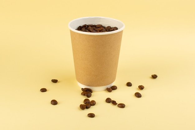 Une tasse de café en plastique vue de face avec des graines de café brun sur le mur jaune