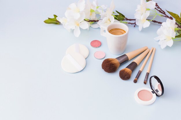 Tasse à café avec des produits cosmétiques et une brindille de fleurs blanches sur fond blanc