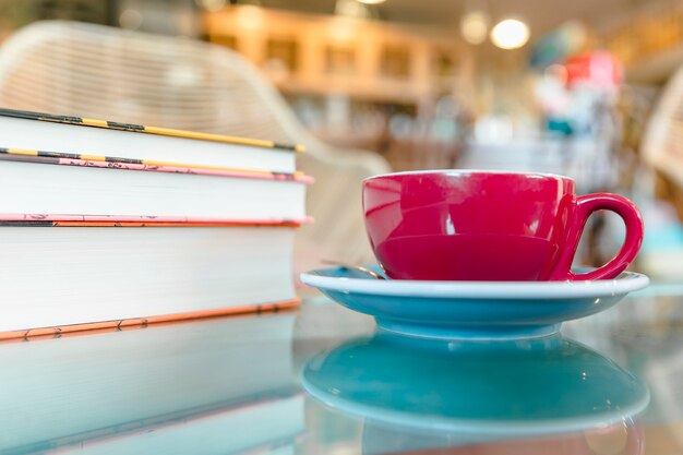 Tasse à café rouge près des livres sur le bureau réfléchissant