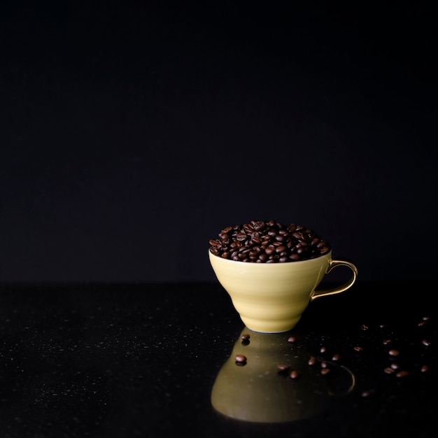 Tasse en céramique remplie de grains de café torréfiés sur fond noir