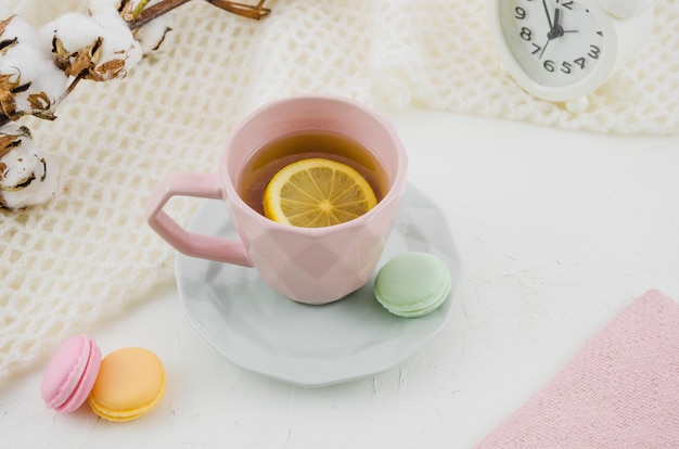 Tasse en céramique rose avec thé au citron et macarons sur fond blanc