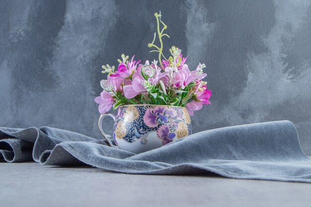 Une tasse de fleurs sur un morceau de tissu, sur le tableau blanc.