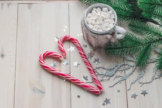 Tasse de guimauves et de cannes de bonbon entouré de décorations de Noël sur une table en bois