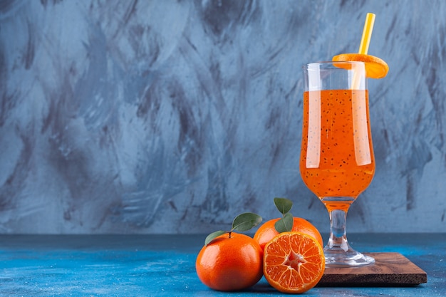 Une tasse de jus en verre avec de la paille et des mandarines entières et tranchées.