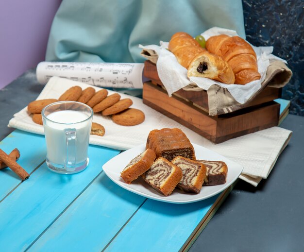 Une tasse de lait avec des croissants et autres pâtisseries sur la table.