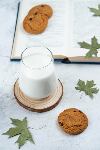 Une tasse de lait en verre avec des biscuits au chocolat sur une planche en bois.