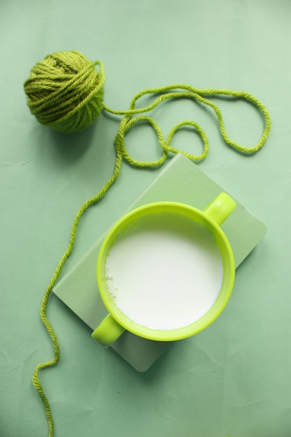 Une tasse de lait verte sur le livre et une boule de fil vert autour de la table verte.