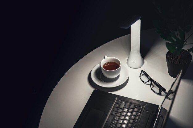 Tasse de lampe à thé et ordinateur portable sur le bureau la nuit