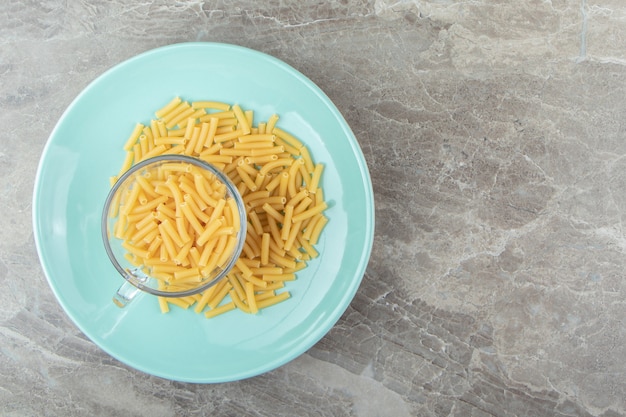 Tasse de macaronis crus sur plaque bleue
