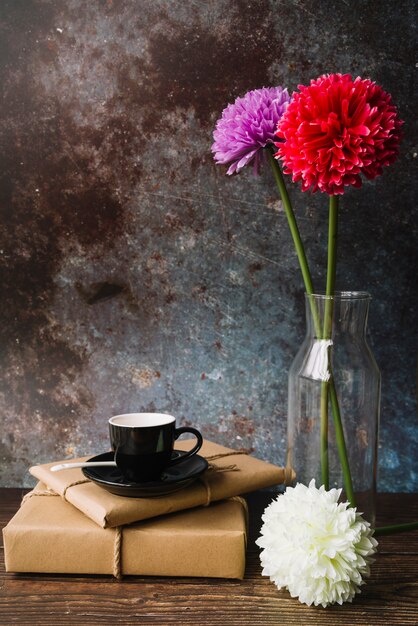 Tasse noire et soucoupe sur des boîtes de cadeau en papier brun emballé avec de belles fleurs